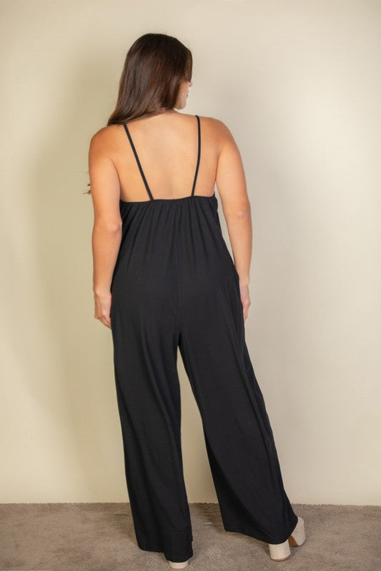 A woman in a Plus Spaghetti Strap Solid Wide Jumpsuit poses against a plain beige background. She has her hands in the pockets and is wearing platform sandals.