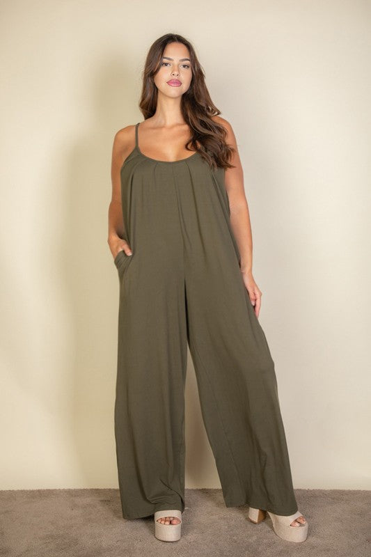 A woman in a Plus Spaghetti Strap Solid Wide Jumpsuit poses against a plain beige background. She has her hands in the pockets and is wearing platform sandals.