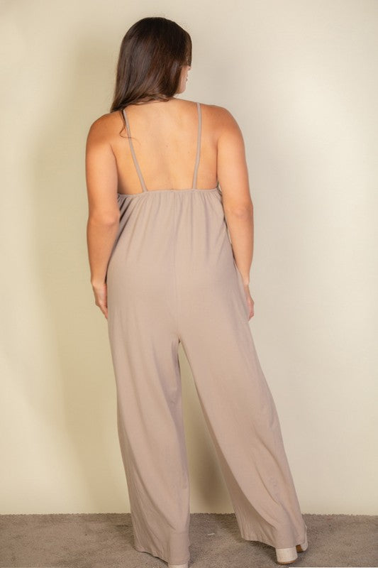 A woman in a Plus Spaghetti Strap Solid Wide Jumpsuit poses against a plain beige background. She has her hands in the pockets and is wearing platform sandals.