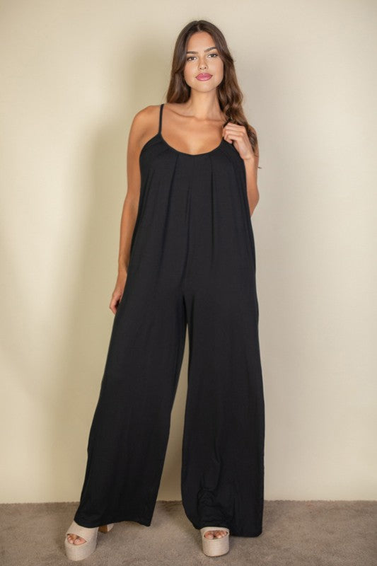 A woman in a Plus Spaghetti Strap Solid Wide Jumpsuit poses against a plain beige background. She has her hands in the pockets and is wearing platform sandals.