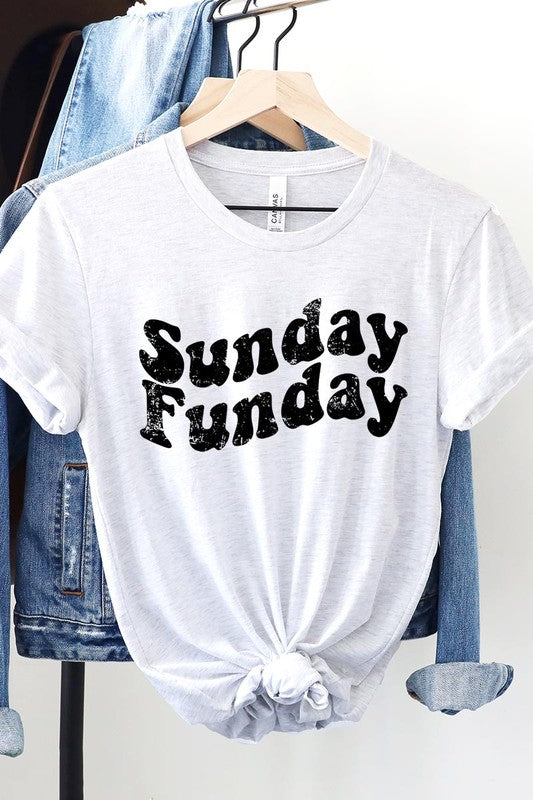 The "Sunday Funday" graphic tee with high-quality direct-to-film printing is paired with light blue distressed denim shorts, a brown hat, and a woven bag on a wooden hanger rack.