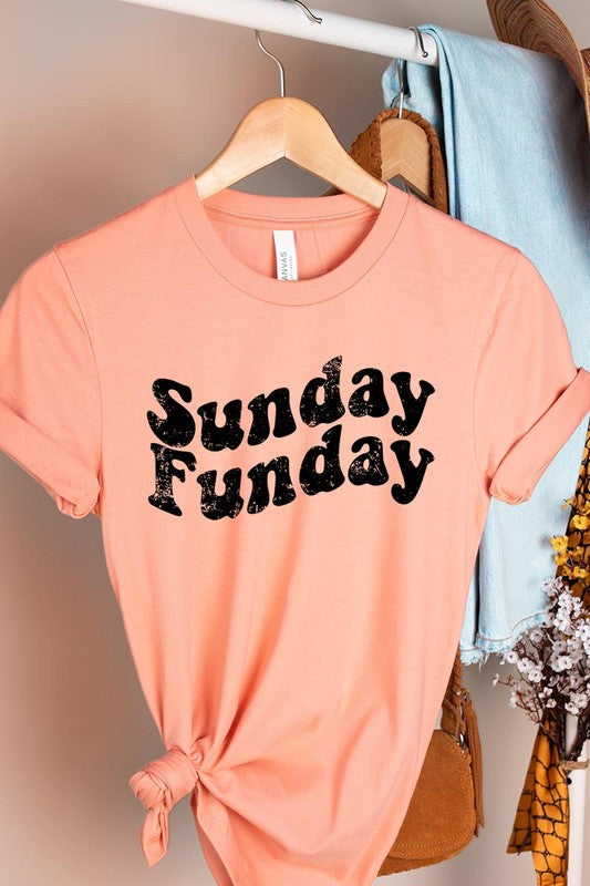 The "Sunday Funday" graphic tee with high-quality direct-to-film printing is paired with light blue distressed denim shorts, a brown hat, and a woven bag on a wooden hanger rack.