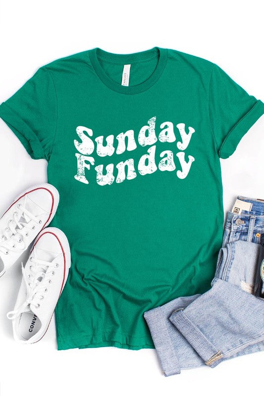 The "Sunday Funday" graphic tee with high-quality direct-to-film printing is paired with light blue distressed denim shorts, a brown hat, and a woven bag on a wooden hanger rack.