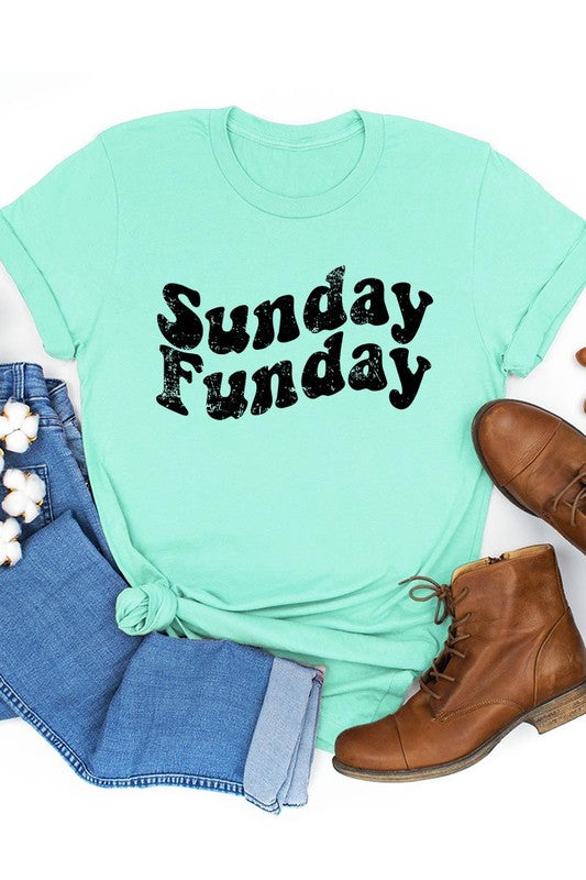 The "Sunday Funday" graphic tee with high-quality direct-to-film printing is paired with light blue distressed denim shorts, a brown hat, and a woven bag on a wooden hanger rack.