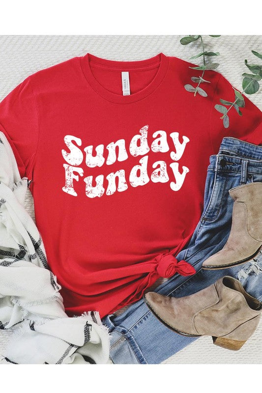 The "Sunday Funday" graphic tee with high-quality direct-to-film printing is paired with light blue distressed denim shorts, a brown hat, and a woven bag on a wooden hanger rack.