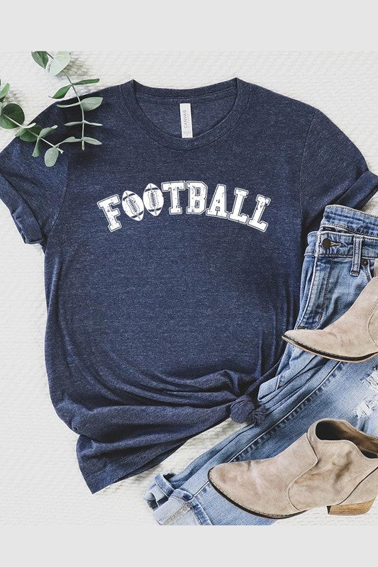 The Football Graphic Tee in beige features "FOOTBALL" in black lettering, paired with light blue distressed denim shorts and a pair of sunglasses. Crafted from premium materials for maximum comfort and style, this unisex crew neck short sleeve shirt is perfect for casual outings.