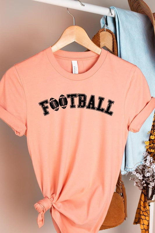 The Football Graphic Tee in beige features "FOOTBALL" in black lettering, paired with light blue distressed denim shorts and a pair of sunglasses. Crafted from premium materials for maximum comfort and style, this unisex crew neck short sleeve shirt is perfect for casual outings.