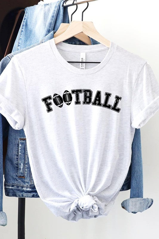 The Football Graphic Tee in beige features "FOOTBALL" in black lettering, paired with light blue distressed denim shorts and a pair of sunglasses. Crafted from premium materials for maximum comfort and style, this unisex crew neck short sleeve shirt is perfect for casual outings.