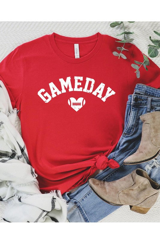 A red Game Day Football Heart Graphic Tee featuring the word "GAMEDAY" with a football inside a heart graphic below it, laid on a white surface paired with blue jeans, a striped scarf, and tan ankle boots. Ideal for Family Group Uniforms on game day!