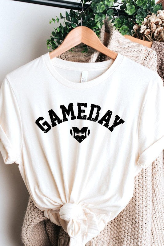 A red Game Day Football Heart Graphic Tee featuring the word "GAMEDAY" with a football inside a heart graphic below it, laid on a white surface paired with blue jeans, a striped scarf, and tan ankle boots. Ideal for Family Group Uniforms on game day!