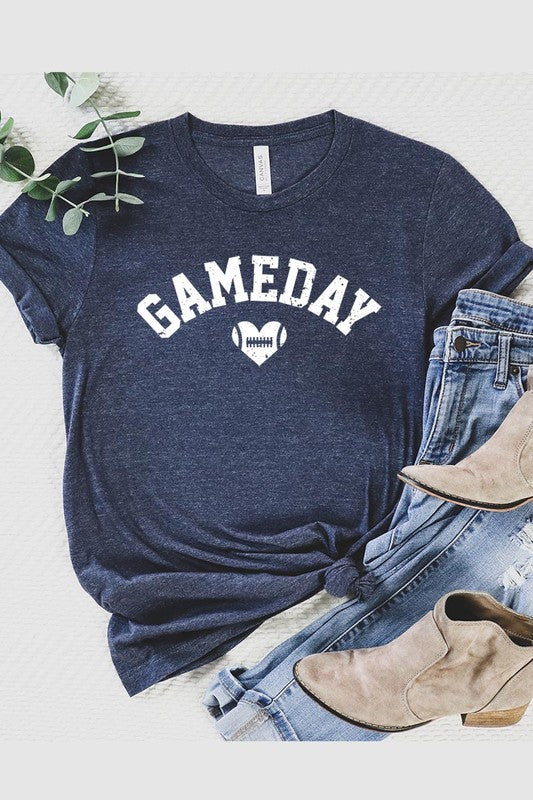 A red Game Day Football Heart Graphic Tee featuring the word "GAMEDAY" with a football inside a heart graphic below it, laid on a white surface paired with blue jeans, a striped scarf, and tan ankle boots. Ideal for Family Group Uniforms on game day!