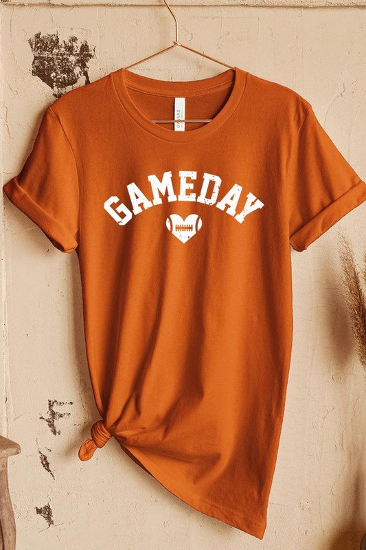 A red Game Day Football Heart Graphic Tee featuring the word "GAMEDAY" with a football inside a heart graphic below it, laid on a white surface paired with blue jeans, a striped scarf, and tan ankle boots. Ideal for Family Group Uniforms on game day!