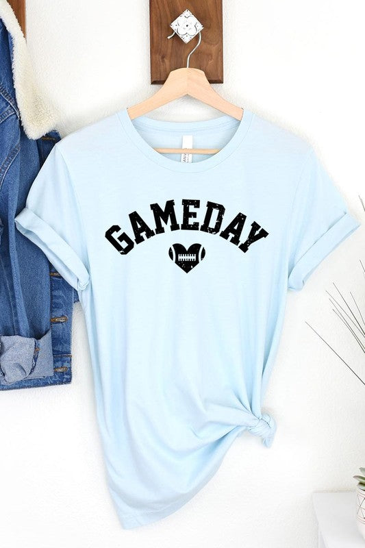 A red Game Day Football Heart Graphic Tee featuring the word "GAMEDAY" with a football inside a heart graphic below it, laid on a white surface paired with blue jeans, a striped scarf, and tan ankle boots. Ideal for Family Group Uniforms on game day!