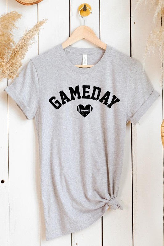 A red Game Day Football Heart Graphic Tee featuring the word "GAMEDAY" with a football inside a heart graphic below it, laid on a white surface paired with blue jeans, a striped scarf, and tan ankle boots. Ideal for Family Group Uniforms on game day!