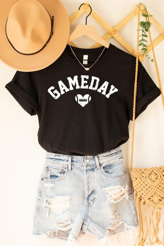 A red Game Day Football Heart Graphic Tee featuring the word "GAMEDAY" with a football inside a heart graphic below it, laid on a white surface paired with blue jeans, a striped scarf, and tan ankle boots. Ideal for Family Group Uniforms on game day!