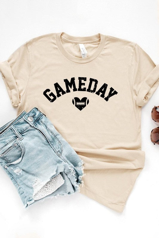 A red Game Day Football Heart Graphic Tee featuring the word "GAMEDAY" with a football inside a heart graphic below it, laid on a white surface paired with blue jeans, a striped scarf, and tan ankle boots. Ideal for Family Group Uniforms on game day!