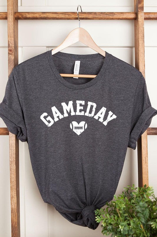 A red Game Day Football Heart Graphic Tee featuring the word "GAMEDAY" with a football inside a heart graphic below it, laid on a white surface paired with blue jeans, a striped scarf, and tan ankle boots. Ideal for Family Group Uniforms on game day!