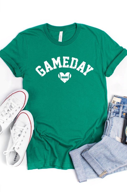 A red Game Day Football Heart Graphic Tee featuring the word "GAMEDAY" with a football inside a heart graphic below it, laid on a white surface paired with blue jeans, a striped scarf, and tan ankle boots. Ideal for Family Group Uniforms on game day!