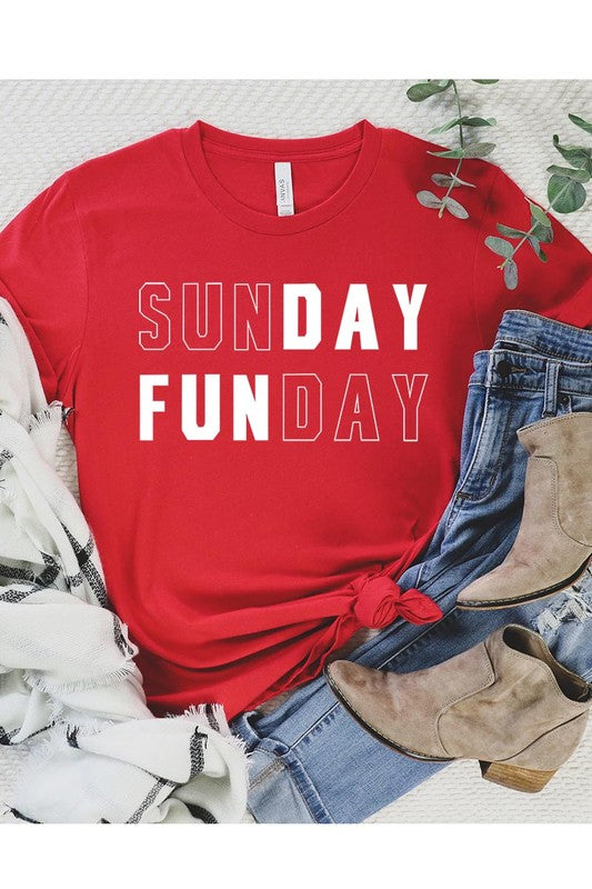 A light pink Sunday Funday Graphic Tee featuring the "SUNDAY FUNDAY" print is hanging on a wooden hanger next to a tan hat and a beige bag filled with flowers. This unisex crew neck short sleeve tee is ideal for family group uniforms.