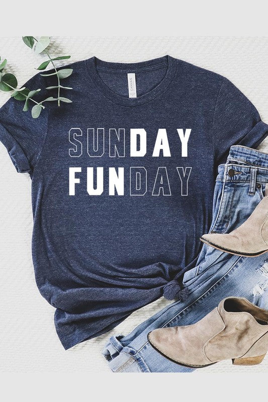 A light pink Sunday Funday Graphic Tee featuring the "SUNDAY FUNDAY" print is hanging on a wooden hanger next to a tan hat and a beige bag filled with flowers. This unisex crew neck short sleeve tee is ideal for family group uniforms.