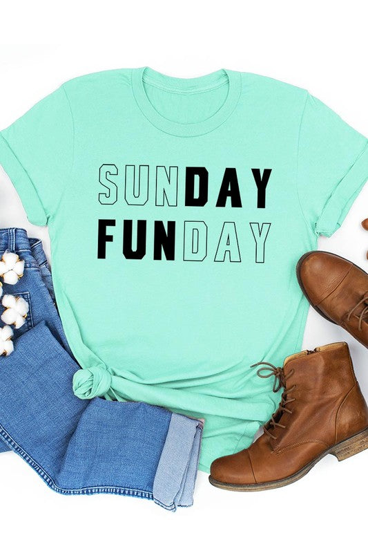 A light pink Sunday Funday Graphic Tee featuring the "SUNDAY FUNDAY" print is hanging on a wooden hanger next to a tan hat and a beige bag filled with flowers. This unisex crew neck short sleeve tee is ideal for family group uniforms.