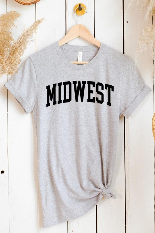 A light pink Unisex Crew Neck Midwest Graphic Tee, featuring rolled sleeves and the word "MIDWEST" printed in bold black letters, hangs on a wooden hanger. This tee makes a perfect addition to your Family Group Uniforms.