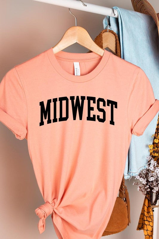 A light pink Unisex Crew Neck Midwest Graphic Tee, featuring rolled sleeves and the word "MIDWEST" printed in bold black letters, hangs on a wooden hanger. This tee makes a perfect addition to your Family Group Uniforms.