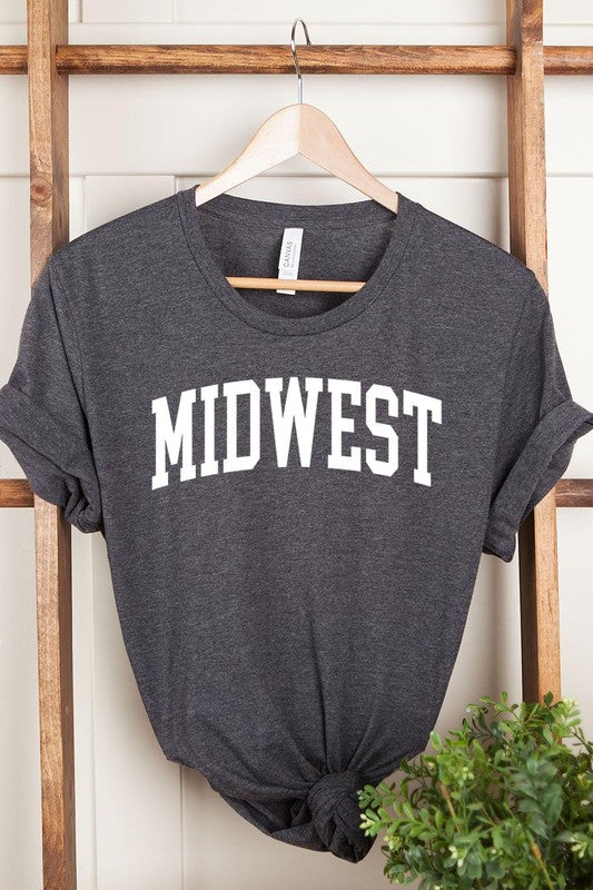 A light pink Unisex Crew Neck Midwest Graphic Tee, featuring rolled sleeves and the word "MIDWEST" printed in bold black letters, hangs on a wooden hanger. This tee makes a perfect addition to your Family Group Uniforms.