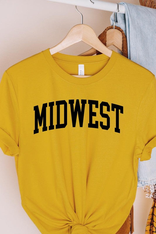 A light pink Unisex Crew Neck Midwest Graphic Tee, featuring rolled sleeves and the word "MIDWEST" printed in bold black letters, hangs on a wooden hanger. This tee makes a perfect addition to your Family Group Uniforms.