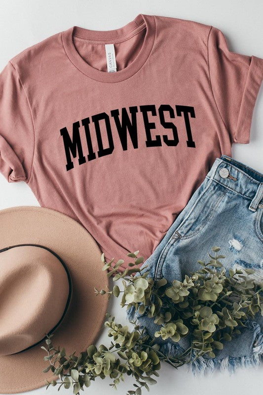 A light pink Unisex Crew Neck Midwest Graphic Tee, featuring rolled sleeves and the word "MIDWEST" printed in bold black letters, hangs on a wooden hanger. This tee makes a perfect addition to your Family Group Uniforms.