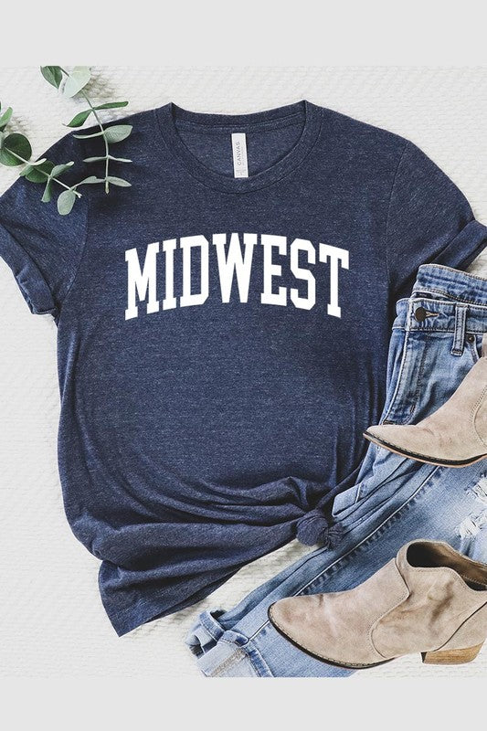 A light pink Unisex Crew Neck Midwest Graphic Tee, featuring rolled sleeves and the word "MIDWEST" printed in bold black letters, hangs on a wooden hanger. This tee makes a perfect addition to your Family Group Uniforms.