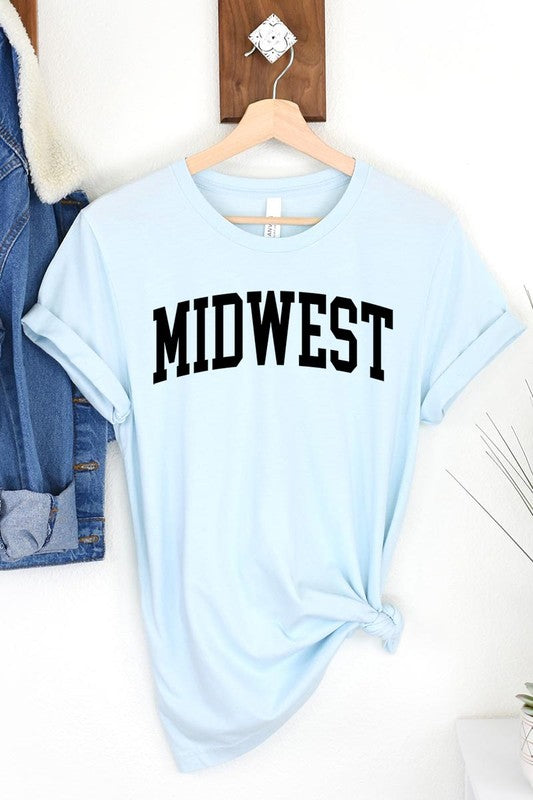 A light pink Unisex Crew Neck Midwest Graphic Tee, featuring rolled sleeves and the word "MIDWEST" printed in bold black letters, hangs on a wooden hanger. This tee makes a perfect addition to your Family Group Uniforms.