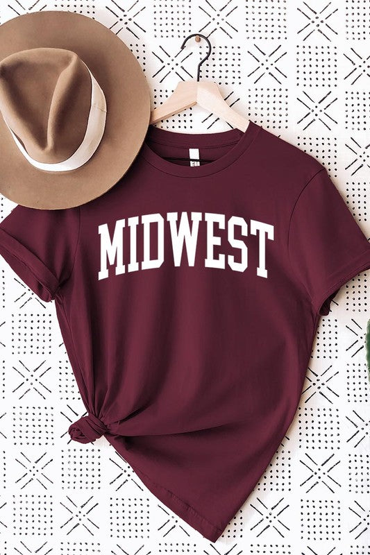 A light pink Unisex Crew Neck Midwest Graphic Tee, featuring rolled sleeves and the word "MIDWEST" printed in bold black letters, hangs on a wooden hanger. This tee makes a perfect addition to your Family Group Uniforms.