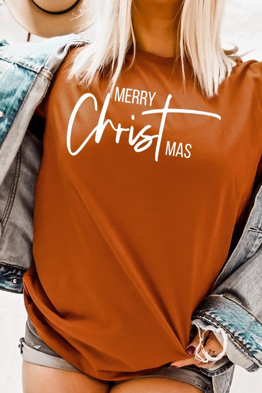 A woman with long blonde hair is smiling while wearing a Merry Christmas Graphic Tee featuring "Merry Christmas" in white script. This unisex crew neck tee boasts a high-quality direct-to-film printed graphic design that ensures vibrant and lasting colors.