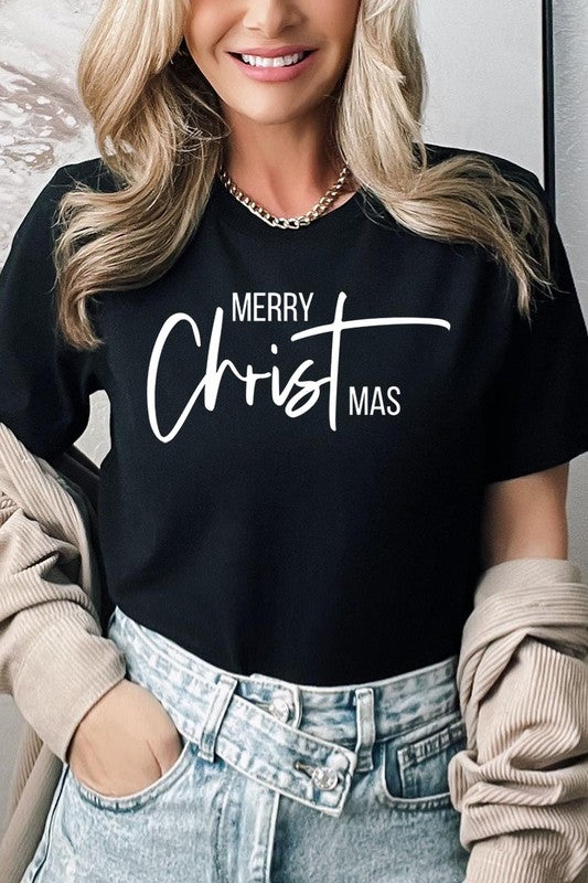 A woman with long blonde hair is smiling while wearing a Merry Christmas Graphic Tee featuring "Merry Christmas" in white script. This unisex crew neck tee boasts a high-quality direct-to-film printed graphic design that ensures vibrant and lasting colors.