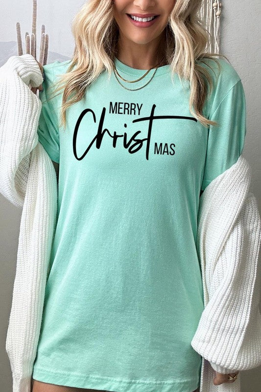 A woman with long blonde hair is smiling while wearing a Merry Christmas Graphic Tee featuring "Merry Christmas" in white script. This unisex crew neck tee boasts a high-quality direct-to-film printed graphic design that ensures vibrant and lasting colors.