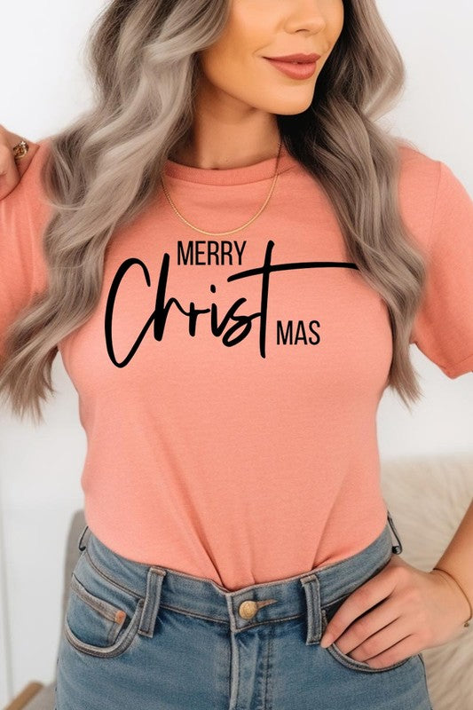 A woman with long blonde hair is smiling while wearing a Merry Christmas Graphic Tee featuring "Merry Christmas" in white script. This unisex crew neck tee boasts a high-quality direct-to-film printed graphic design that ensures vibrant and lasting colors.