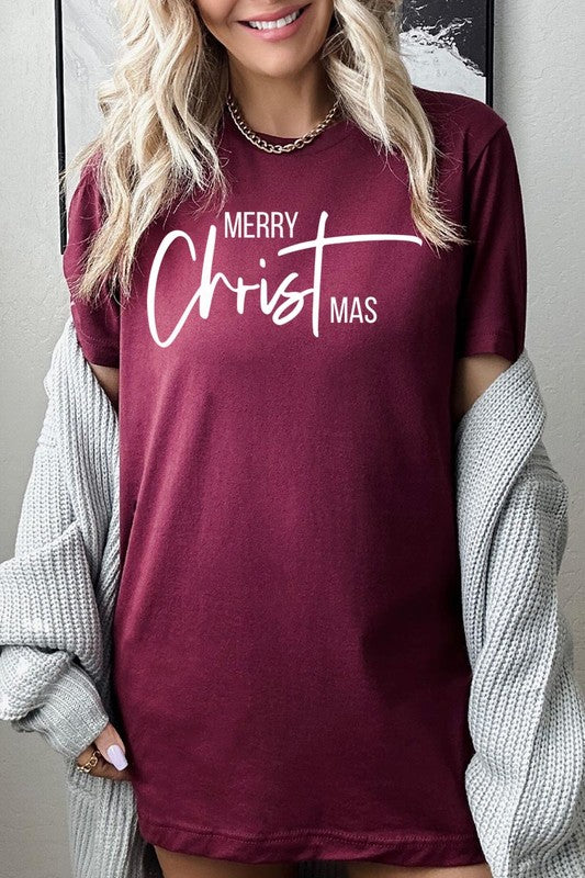 A woman with long blonde hair is smiling while wearing a Merry Christmas Graphic Tee featuring "Merry Christmas" in white script. This unisex crew neck tee boasts a high-quality direct-to-film printed graphic design that ensures vibrant and lasting colors.