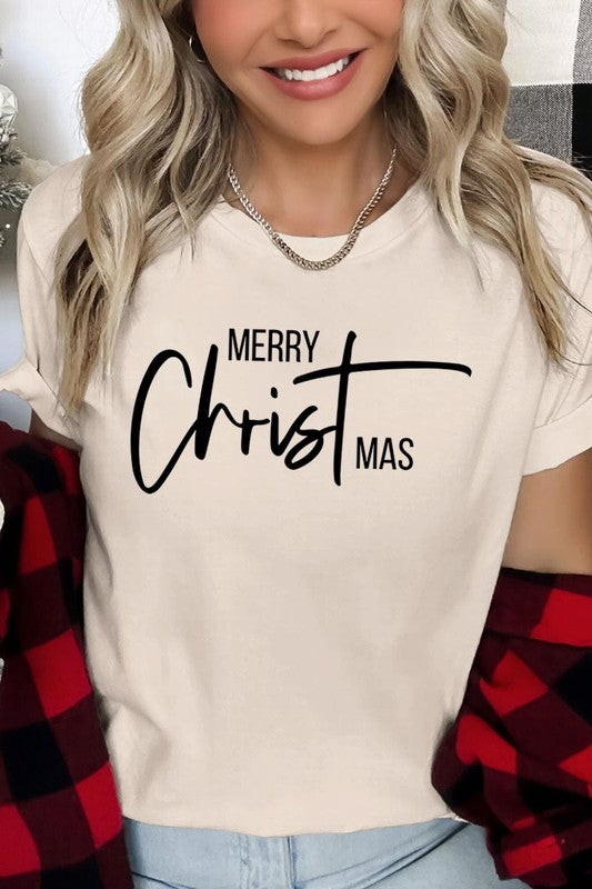 A woman with long blonde hair is smiling while wearing a Merry Christmas Graphic Tee featuring "Merry Christmas" in white script. This unisex crew neck tee boasts a high-quality direct-to-film printed graphic design that ensures vibrant and lasting colors.