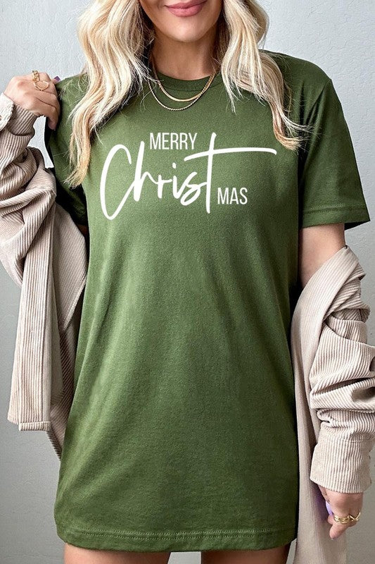 A woman with long blonde hair is smiling while wearing a Merry Christmas Graphic Tee featuring "Merry Christmas" in white script. This unisex crew neck tee boasts a high-quality direct-to-film printed graphic design that ensures vibrant and lasting colors.