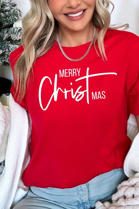 A woman with long blonde hair is smiling while wearing a Merry Christmas Graphic Tee featuring "Merry Christmas" in white script. This unisex crew neck tee boasts a high-quality direct-to-film printed graphic design that ensures vibrant and lasting colors.