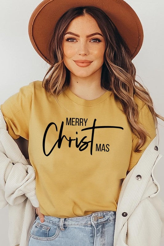 A woman with long blonde hair is smiling while wearing a Merry Christmas Graphic Tee featuring "Merry Christmas" in white script. This unisex crew neck tee boasts a high-quality direct-to-film printed graphic design that ensures vibrant and lasting colors.