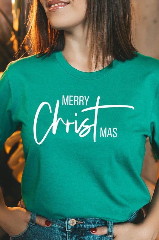 A woman with long blonde hair is smiling while wearing a Merry Christmas Graphic Tee featuring "Merry Christmas" in white script. This unisex crew neck tee boasts a high-quality direct-to-film printed graphic design that ensures vibrant and lasting colors.