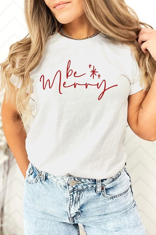 A person wearing the stylish and high-quality Be Merry Graphic Tee, featuring a decorative design with light-colored fabric and bold red text that reads "Be Merry." The unisex crew neck shirt is perfectly paired with them holding a red and black plaid garment.