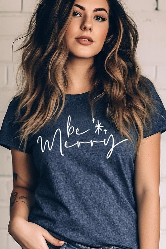 A person wearing the stylish and high-quality Be Merry Graphic Tee, featuring a decorative design with light-colored fabric and bold red text that reads "Be Merry." The unisex crew neck shirt is perfectly paired with them holding a red and black plaid garment.