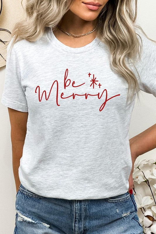 A person wearing the stylish and high-quality Be Merry Graphic Tee, featuring a decorative design with light-colored fabric and bold red text that reads "Be Merry." The unisex crew neck shirt is perfectly paired with them holding a red and black plaid garment.