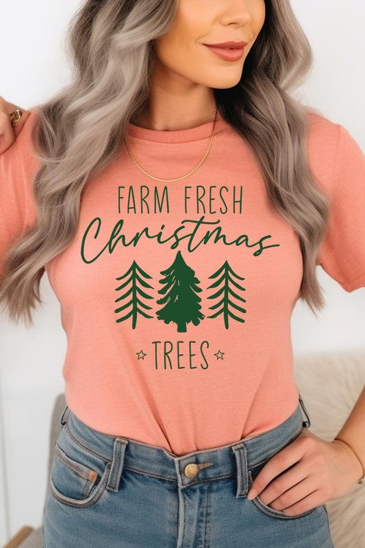 A woman wearing the "Farm Fresh Christmas Trees Graphic Tee" in green, adorned with white text and tree graphics.