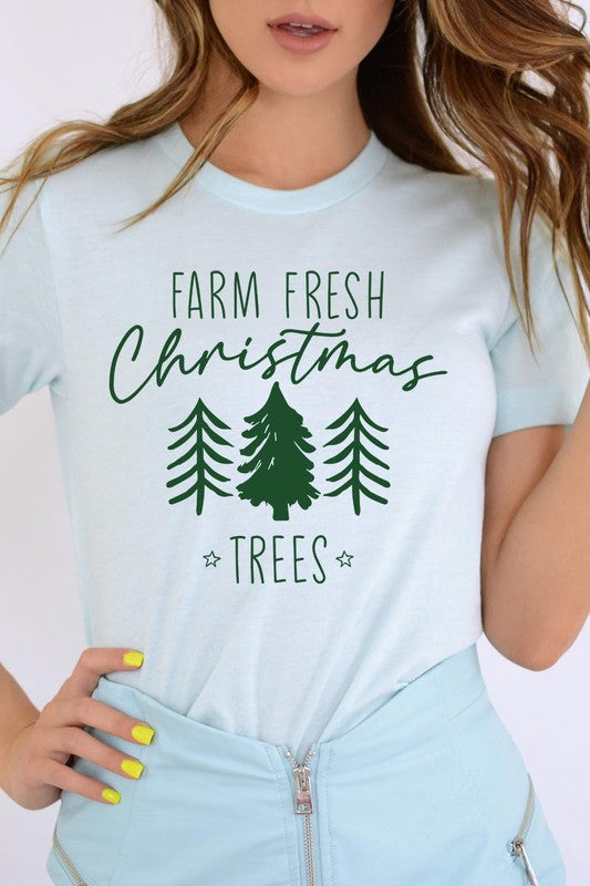 A woman wearing the "Farm Fresh Christmas Trees Graphic Tee" in green, adorned with white text and tree graphics.