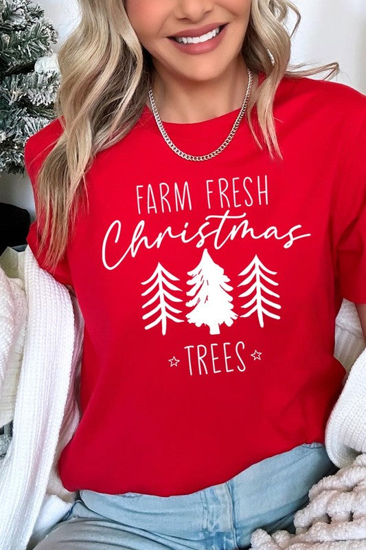 A woman wearing the "Farm Fresh Christmas Trees Graphic Tee" in green, adorned with white text and tree graphics.