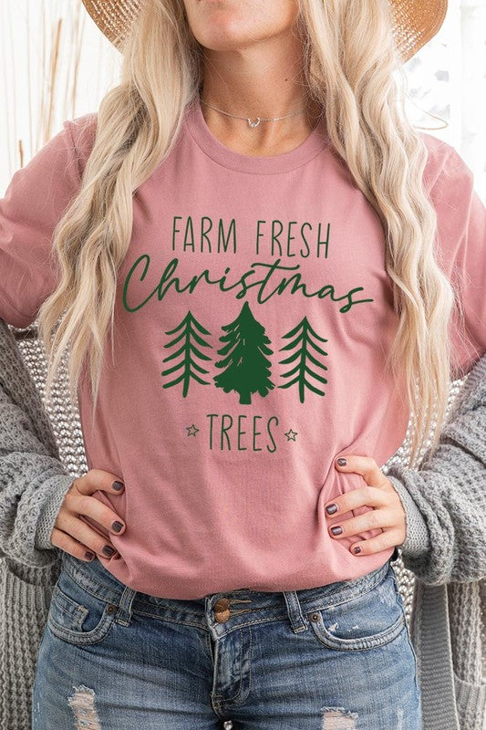 A woman wearing the "Farm Fresh Christmas Trees Graphic Tee" in green, adorned with white text and tree graphics.